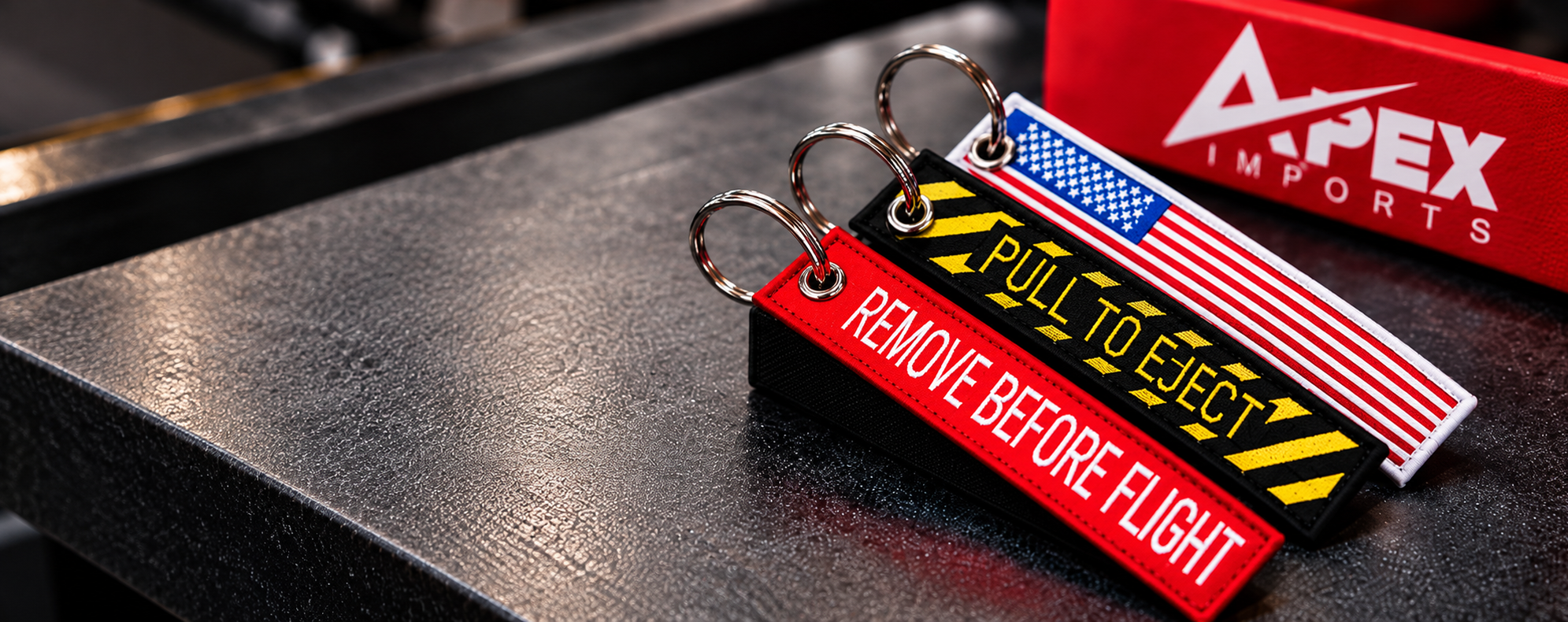 Embroidered keychains beside an Apex Imports box